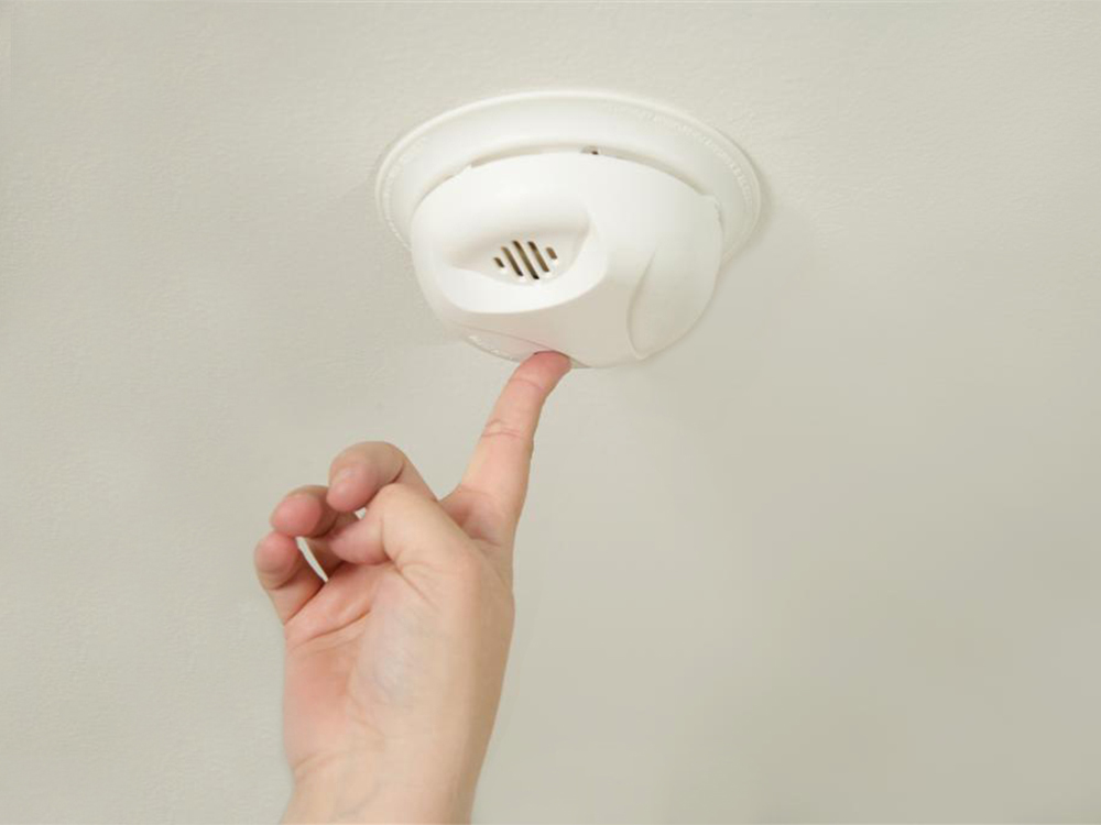 a finger pushing a smoke detetor on the ceiling